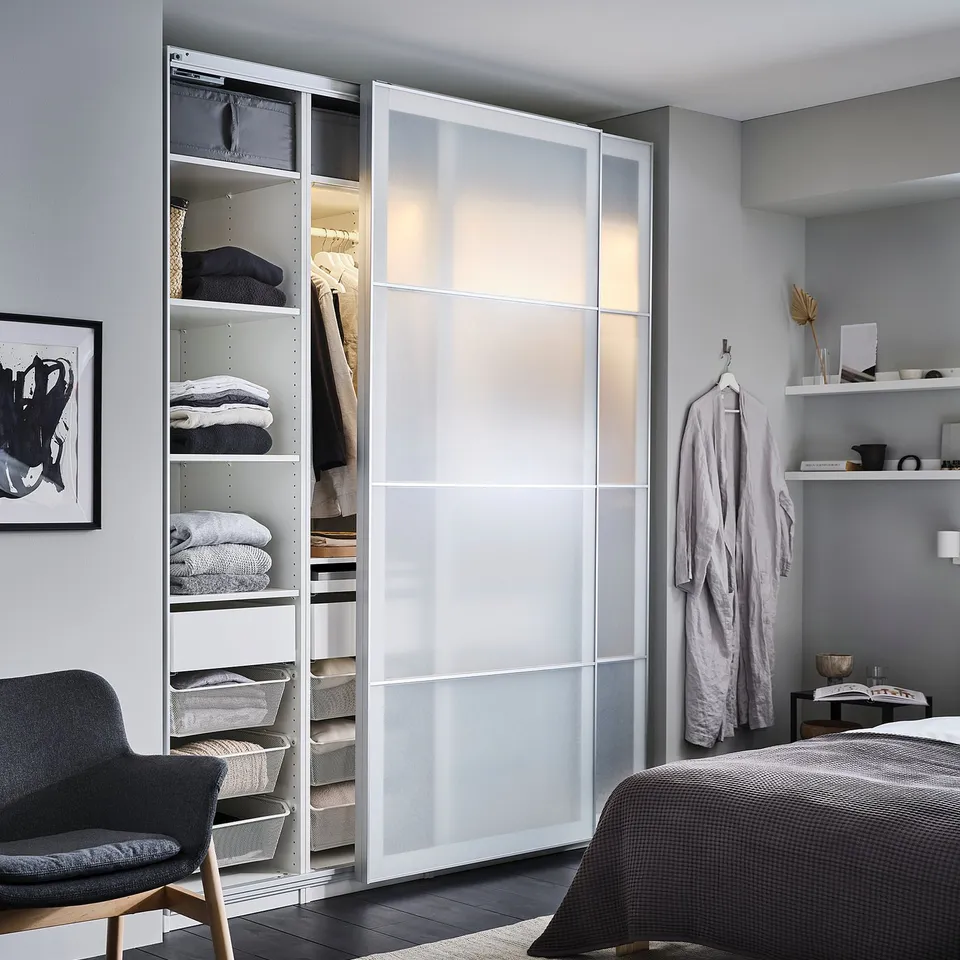 Modern grey bedroom with PAX wardrobe, white sliding doors, dark grey bed, black chair, and minimalist decor.