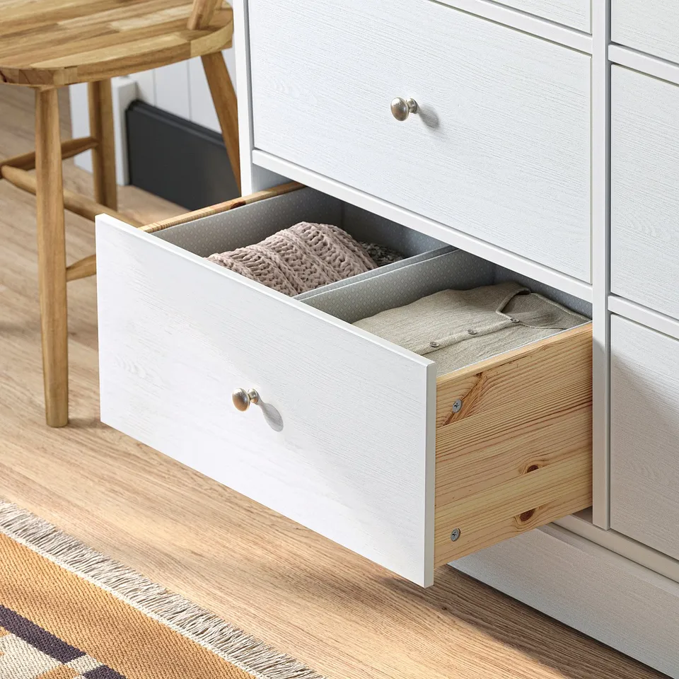 A white HAVSTA dresser with one drawer open, showing folded clothes in a bedroom setting.