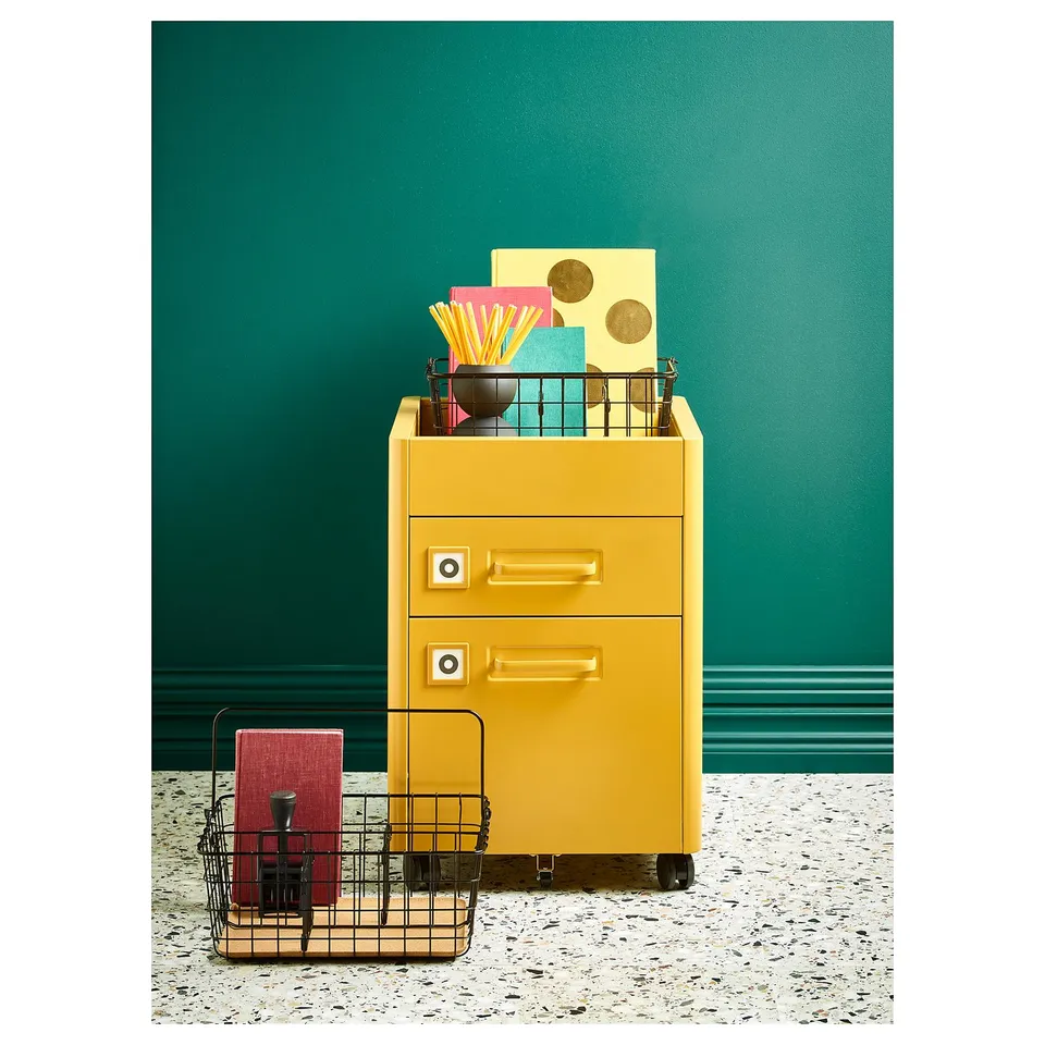 Bright yellow IDÅSEN filing cabinet with drawers, metal mesh baskets, and colourful office supplies.