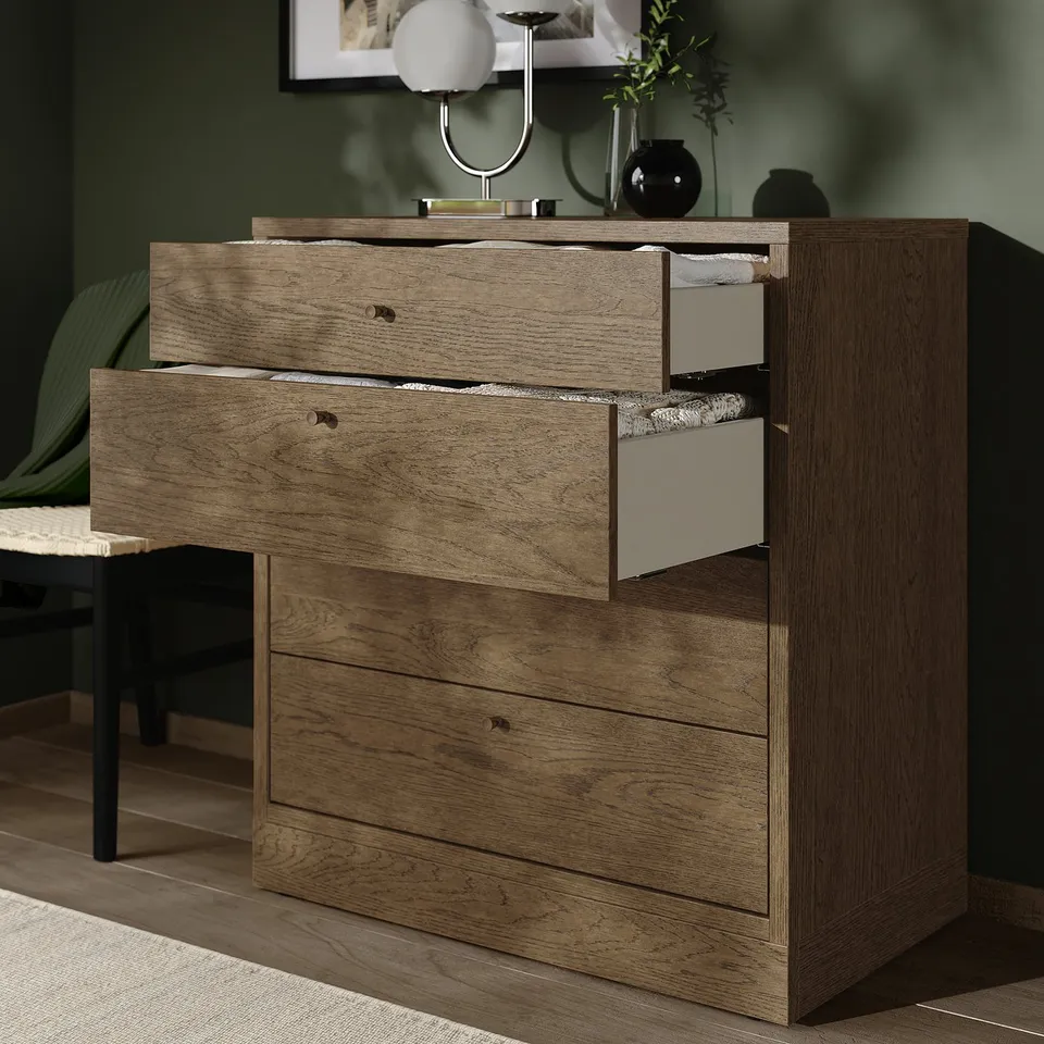 Wooden dresser with 4 drawers, 3 open showing items inside. White and grey inner drawers, -knobs. Decorative lamp and plants on top.