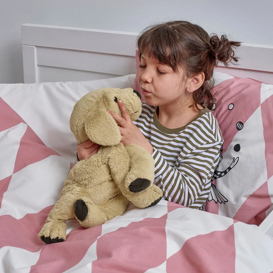 Young girl sleeping on bed, holding a cuddly toy. The toy is soft, huggable, and designed for comfort.