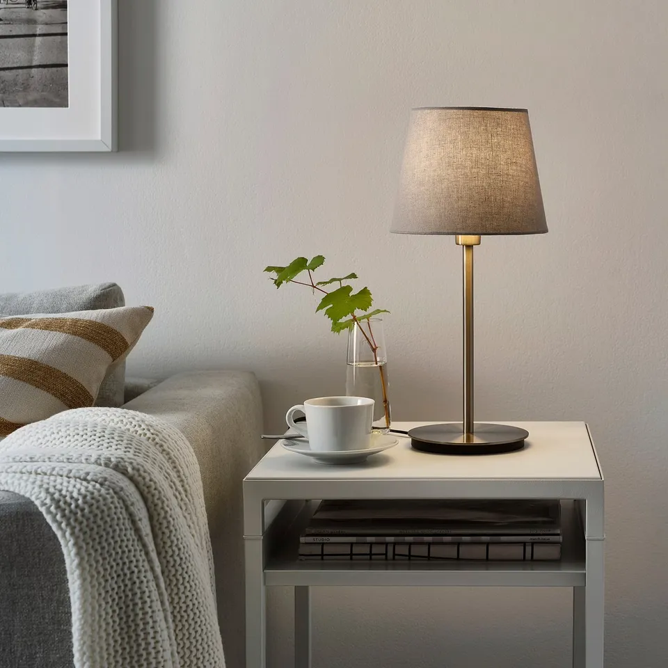 Small, stylish SKAFTET lamp on table, grey, modern design, near couch.