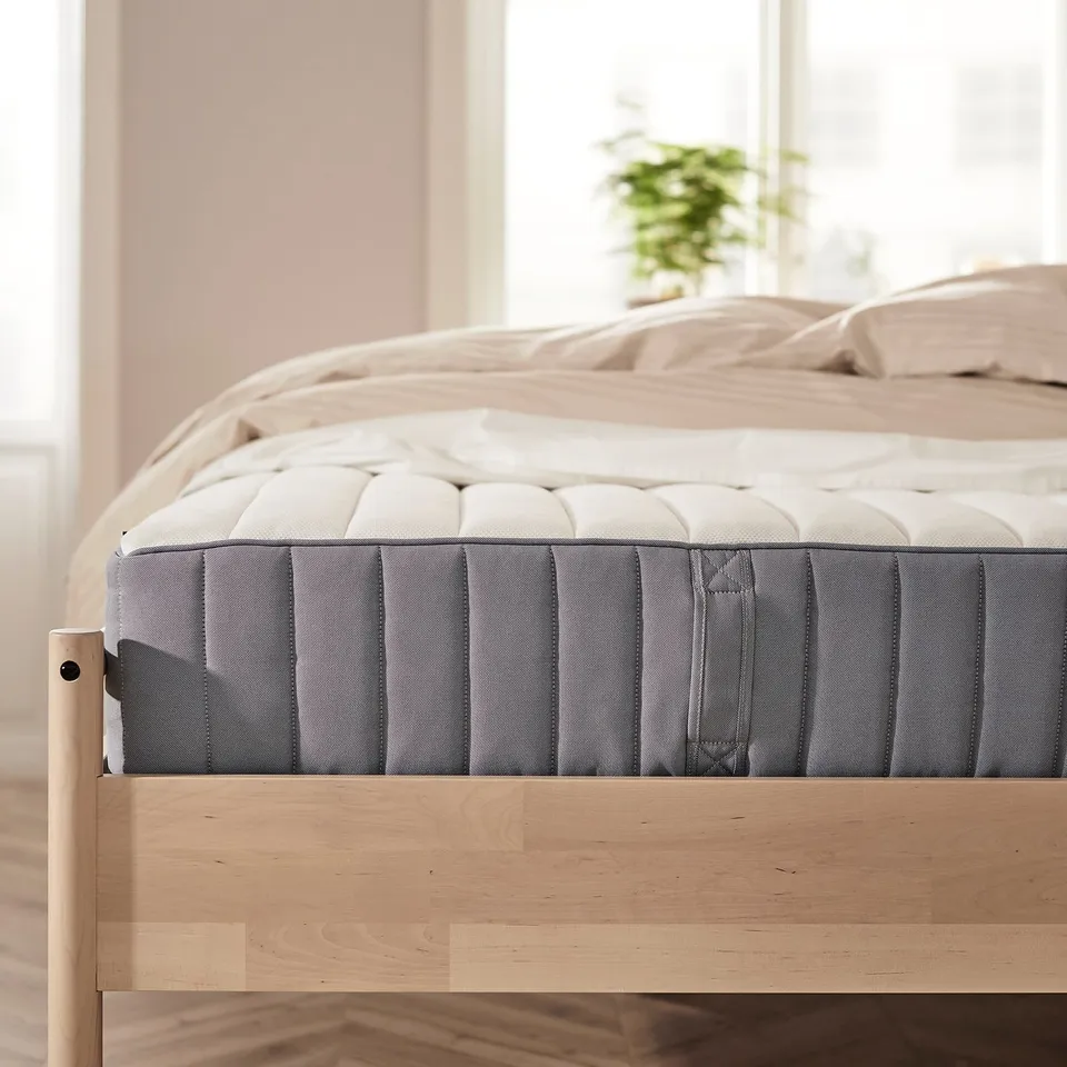 Modern wooden bed with grey pocket sprung mattress in light bedroom.