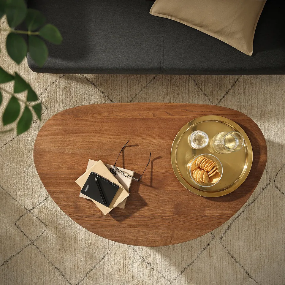 ÖRTRÄSK oval wooden coffee table with warm finish, books and snacks on a rug - cosy setting.