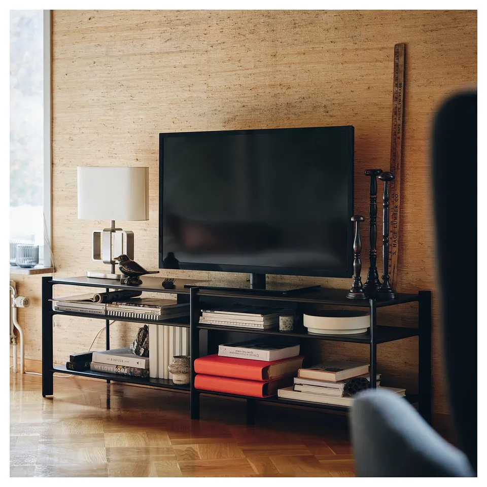 Modern black tv stand with bamboo shelves, holding a flat screen tv, books, and decorations against a textured wall.