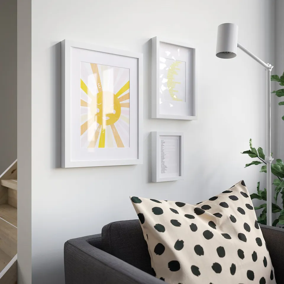 Yellow sun print in white frame on bright wall, with sofa and plant.