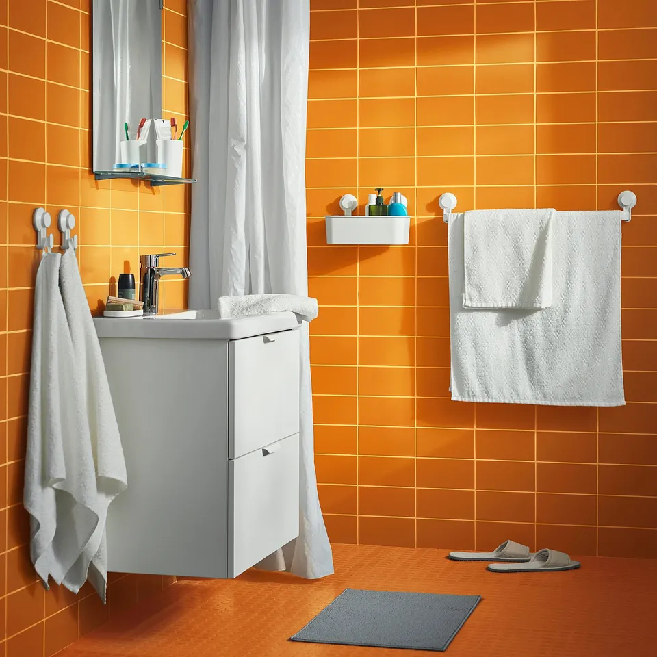 Bright orange-tiled modern bathroom with white accessories, including a sink, mirror, towels, and cosy grey slippers.