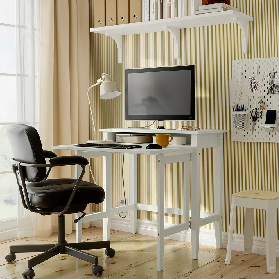 Gullberg desk in home office with chair, stool, tv, lamp, & pegboard.