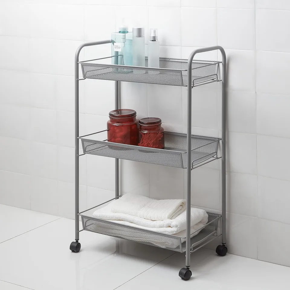 Silver HORNAVAN 3-tier metal bathroom trolley with black wheels holds towels, bottles, and jars; against white tiles.