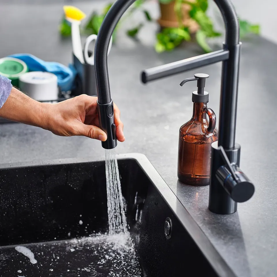 A person turns on a modern black kitchen tap with a pull-down spray. Water flows into the sink.