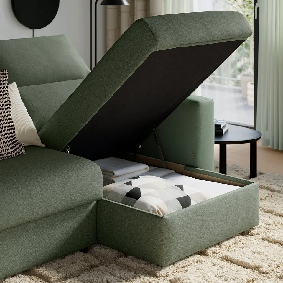 Green sofa with storage, cushions, and pillows. One seat is open, revealing blankets and pillows inside.
