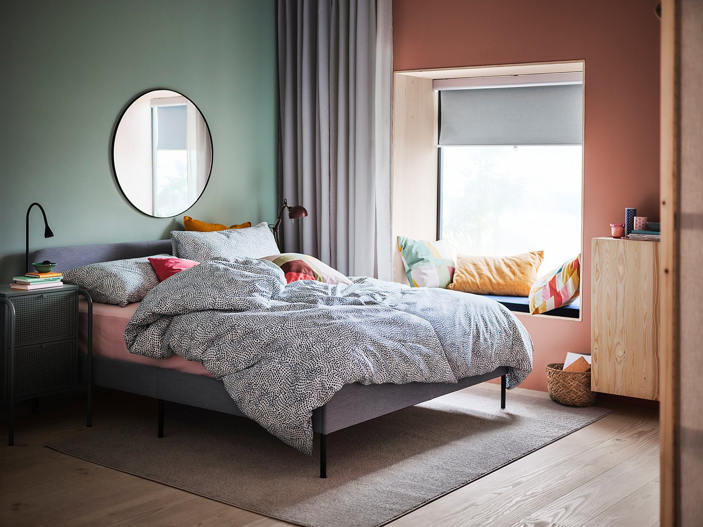 Cosy bedroom with black-framed round mirror, colourful pillows, and wooden furniture.