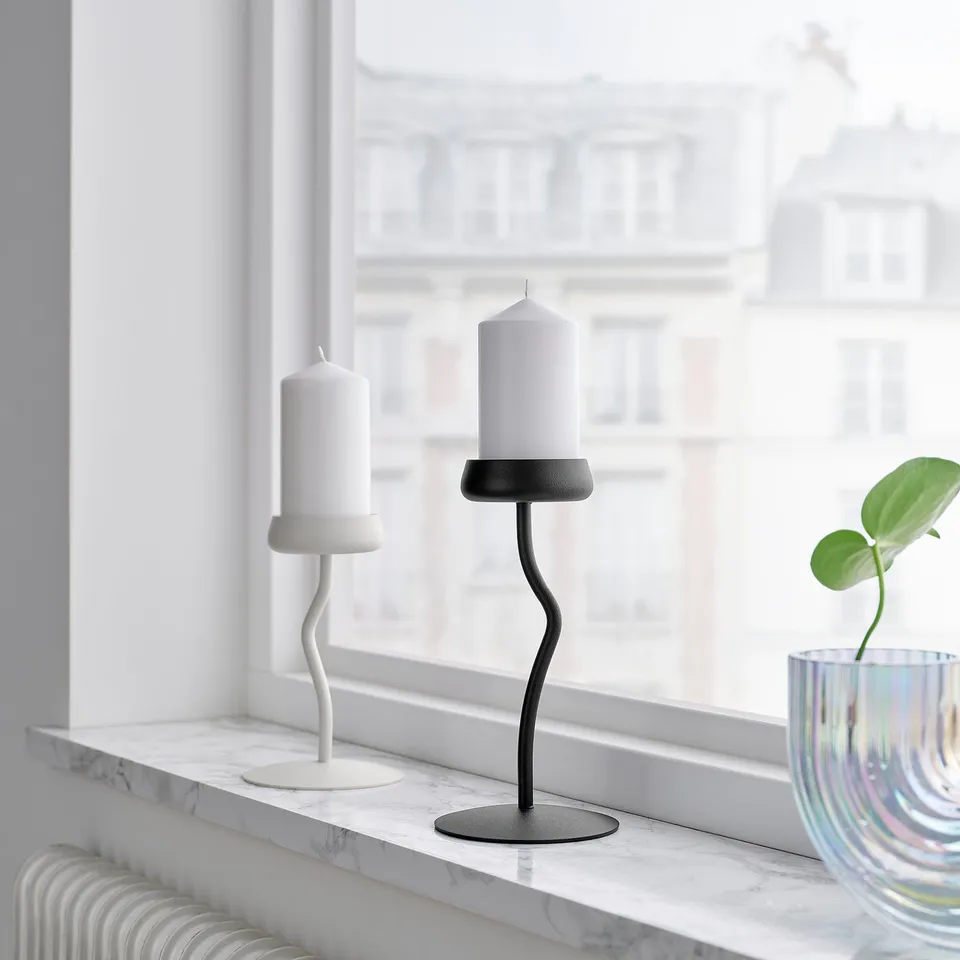 Black and white candle holders on marble windowsill with plant in blue vase.