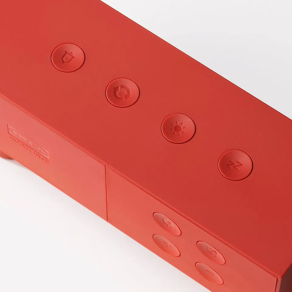Red portable speaker with embossed buttons: play, pause, volume, and power.
