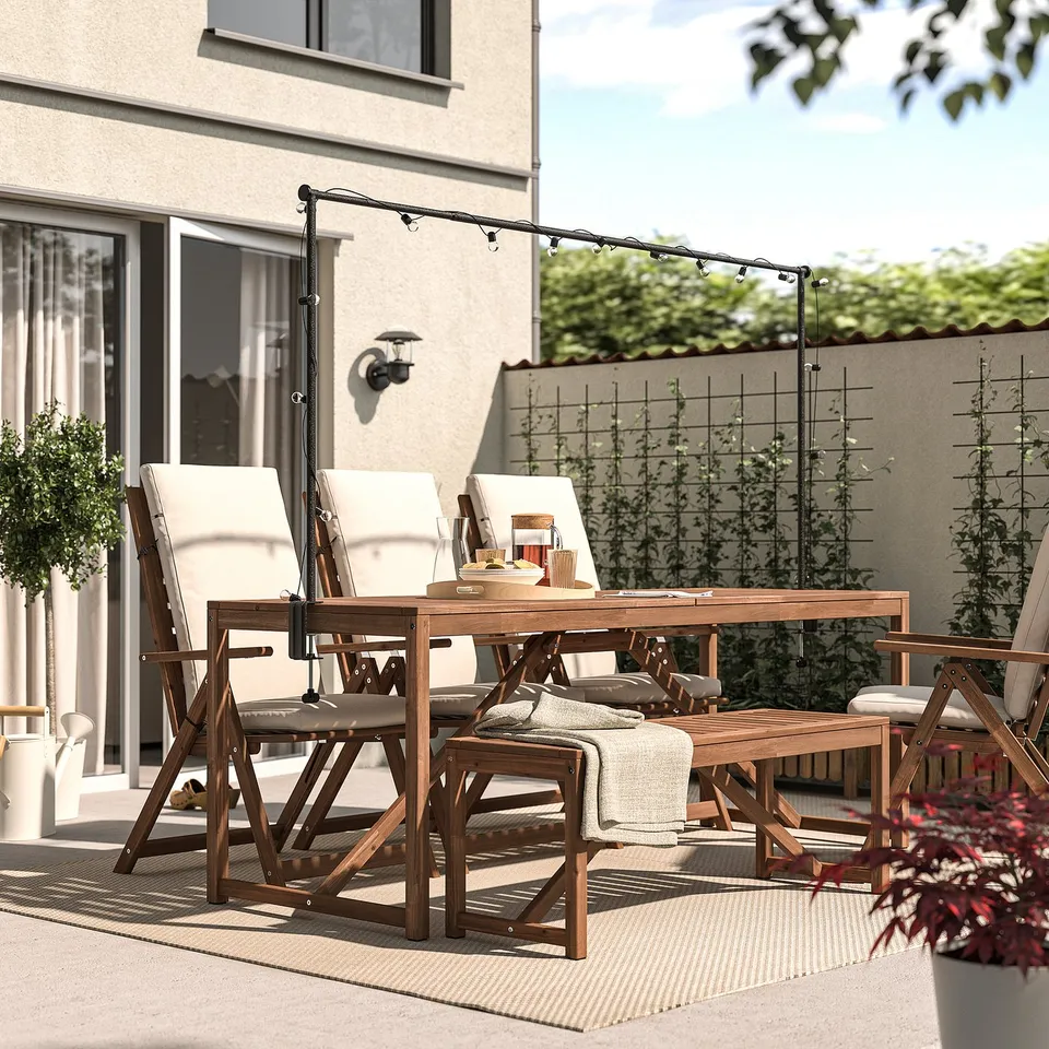 Outdoor dining set with wooden table, four chairs, and bench. String lights and relaxed seating, perfect for casual evenings.
