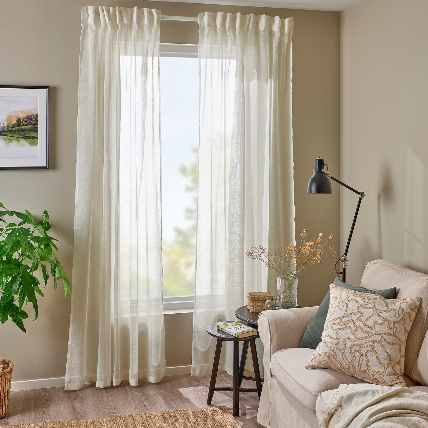 Modern living room with HÄLLEBRÄCKA curtains, soft light, chair, cushions, plant, and lamp.