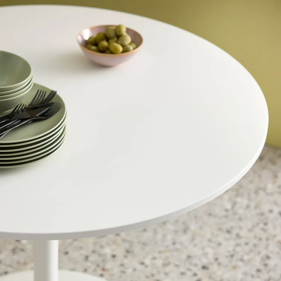 A round DOCKSTA table with green plates, black cutlery, and olives.