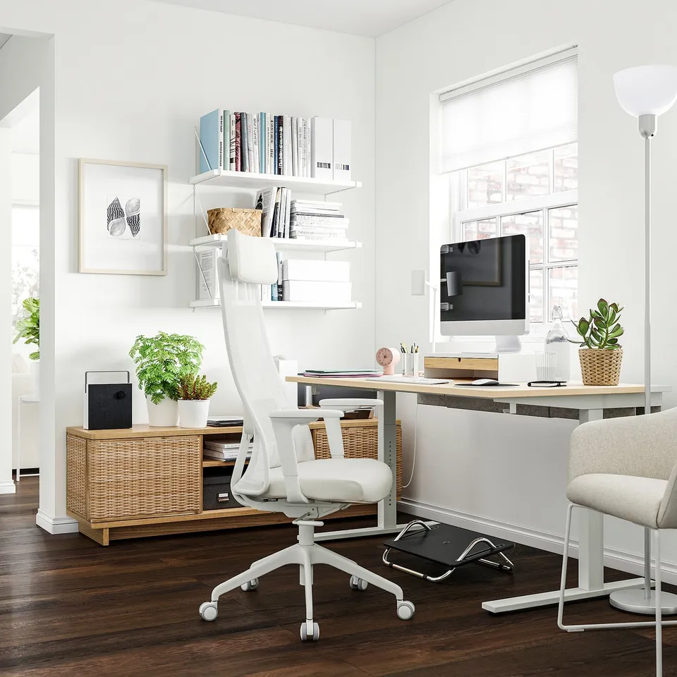 Bright, minimalist home office with white MITTZON desk, ergonomic chair, wooden cabinet, plants, and shelves with books.