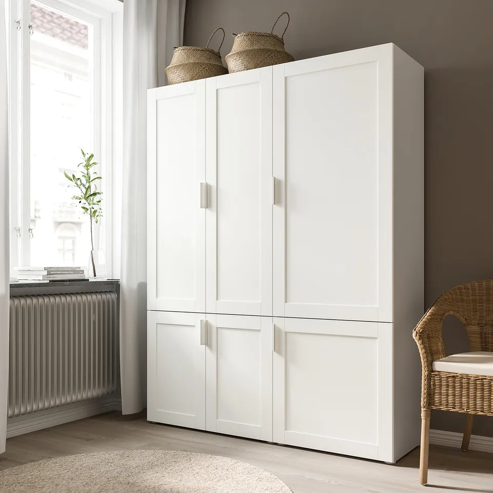 White SANNIDAL cabinet with four doors, two baskets on top, wicker chair beside, and plant beside window.