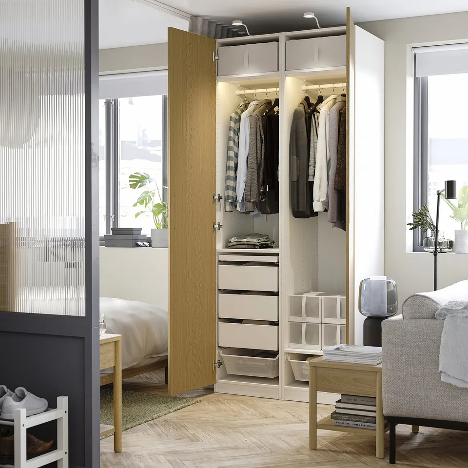 Open wardrobe showcasing clothes, drawers, and storage solutions. Interior lighting highlights organised garments and accessories.