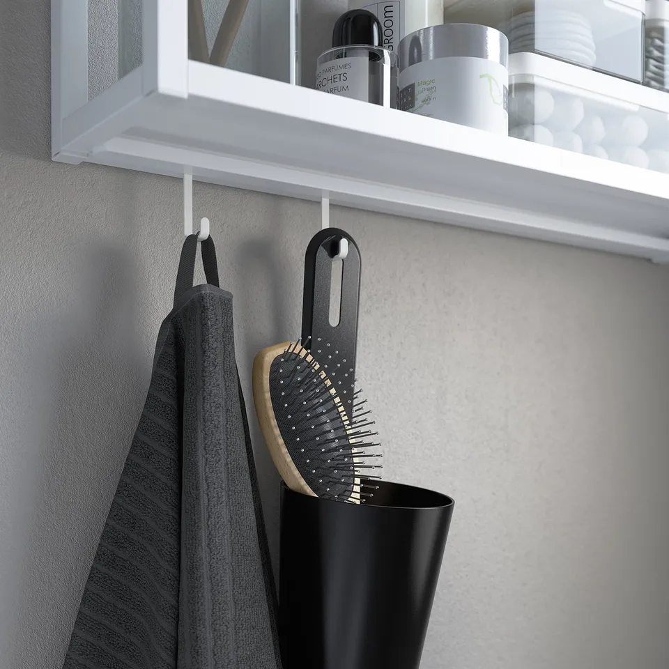 Black hairbrush hangs in bathroom. White shelf above holds bottles, towel hangs below.
