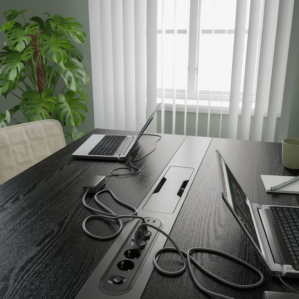 Slate-colored conference table with laptops and chargers in a well-lit room, showcasing its functional cable management module for easy connectivity.