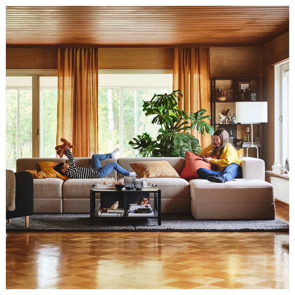 Two people on beige sofa in cosy, wooden room with large windows.