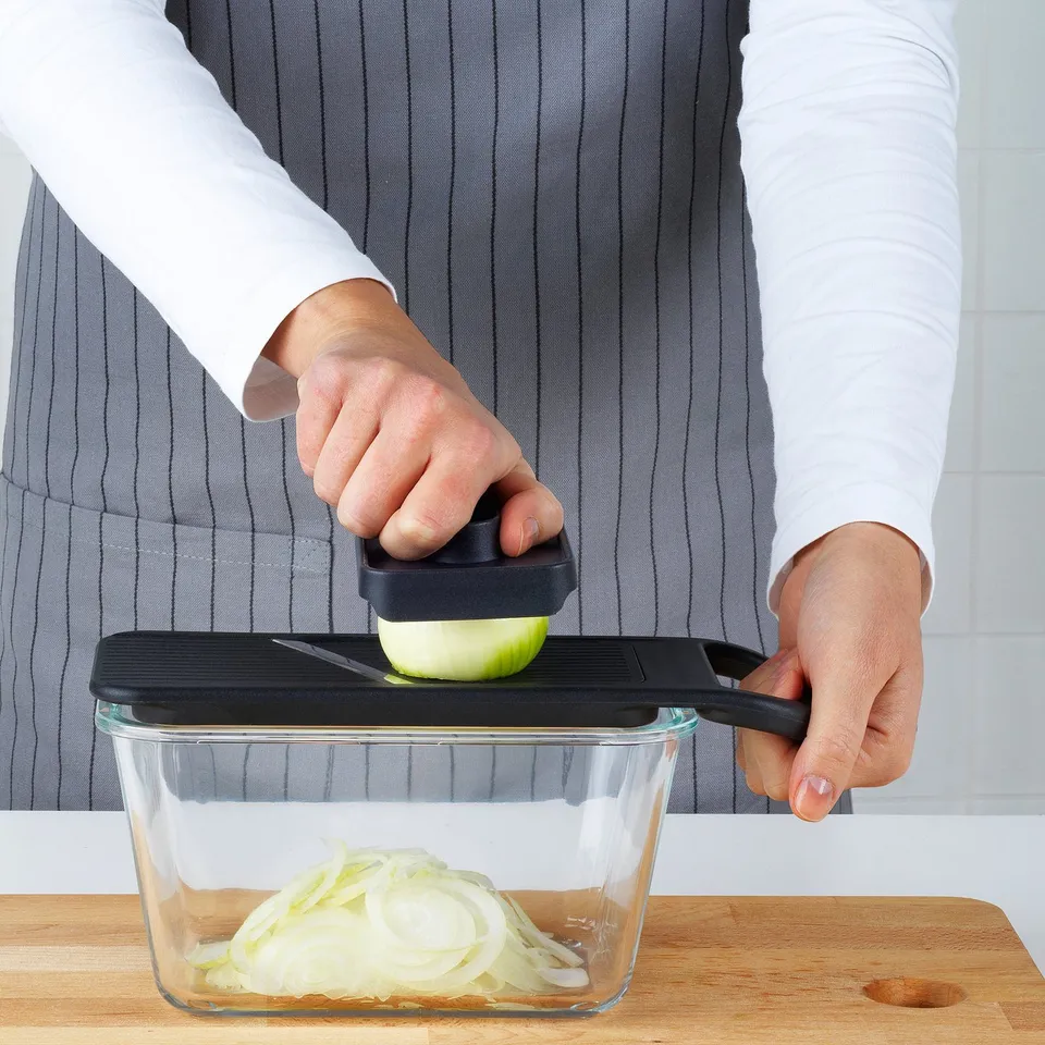 Person using IKEA 365+ mandoline to slice onions into a container.