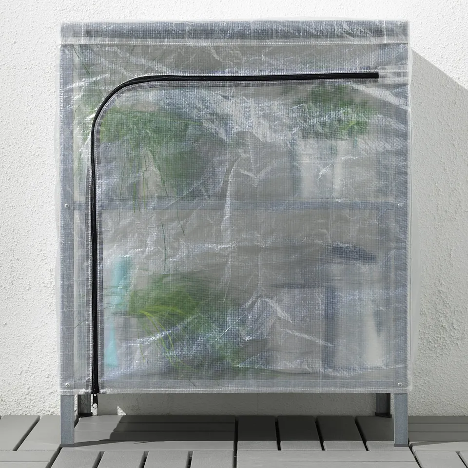 A transparent plastic cover on a shelving unit, likely used as a mini greenhouse. It protects contents from dust and allows air circulation.