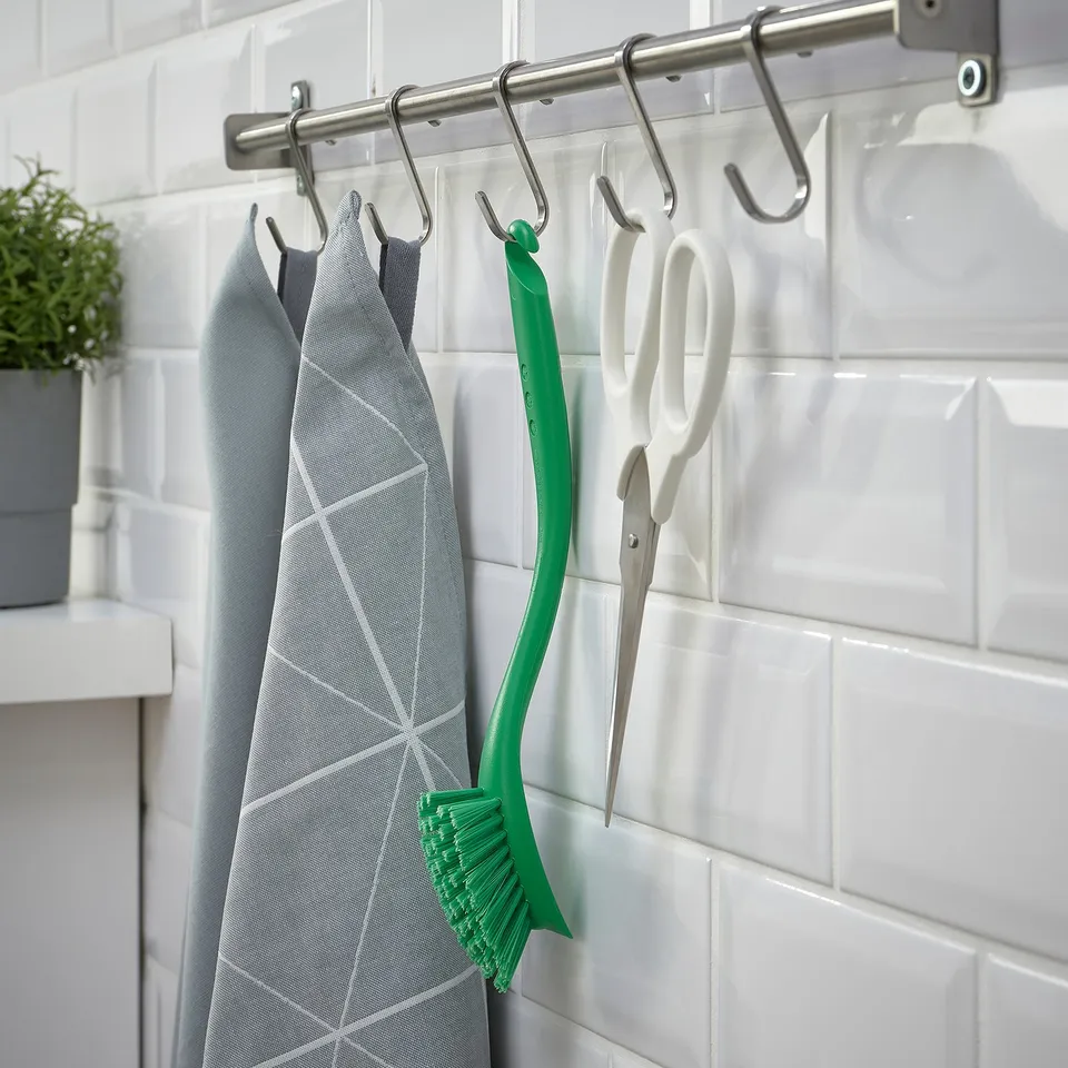 A kitchen rack with hanging utensils, including grey towels, green dish brush, and white scissors.
