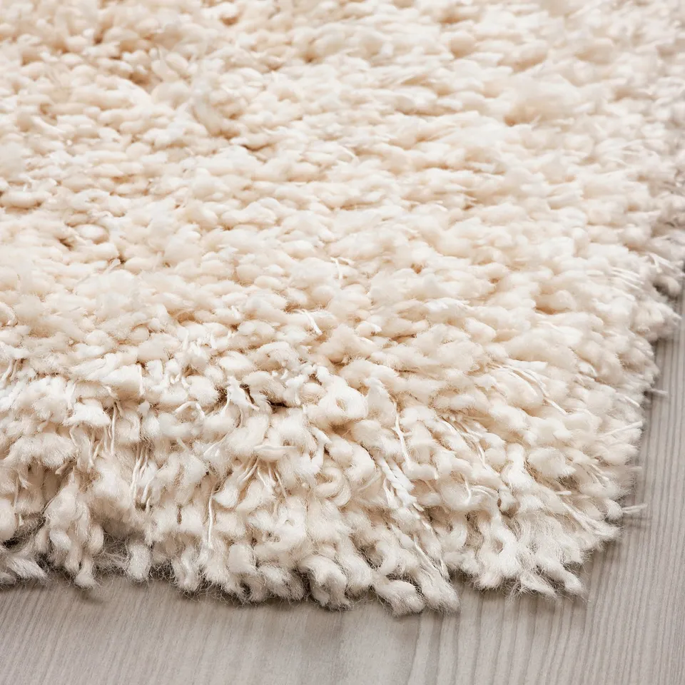 Close-up of thick, shaggy white rug. Soft, textured yarns, laid on wooden floor.