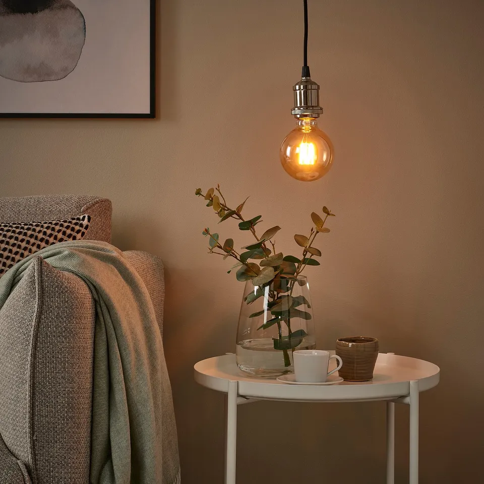 Cosy corner with hanging lamp, amber bulb, plush textiles, and foliage.