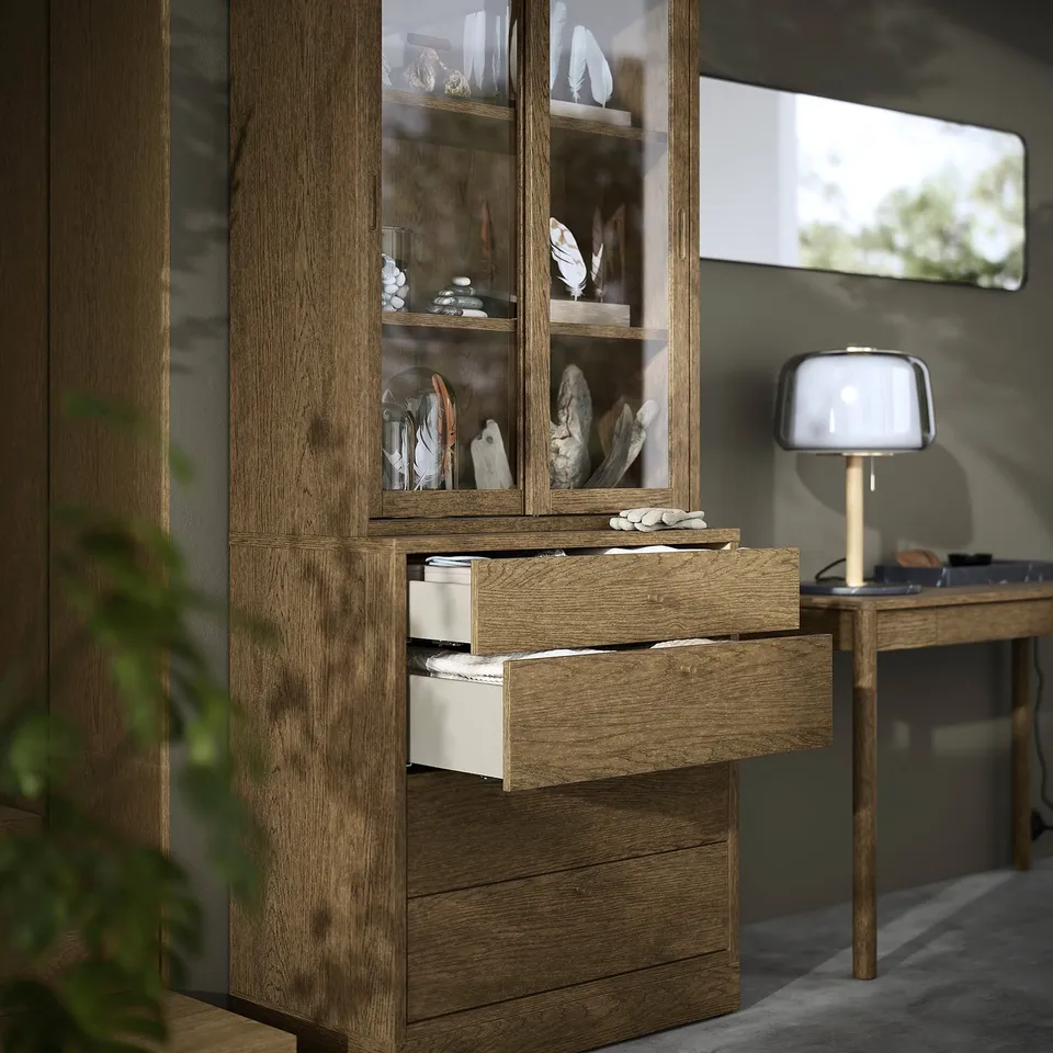 Wooden cabinet with glass doors showcasing decorative items. Two bottom drawers are open, revealing organised storage.