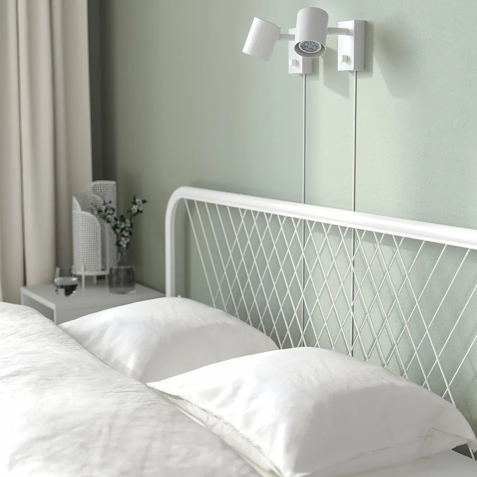 Modern bedroom with white metal bed, net headboard, wall light on sage green wall.