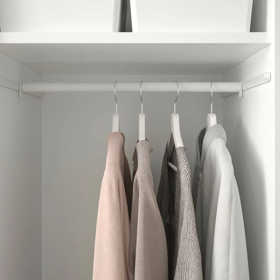 Closet with white clothes rail, holding several hangers with sweaters, organised neatly.