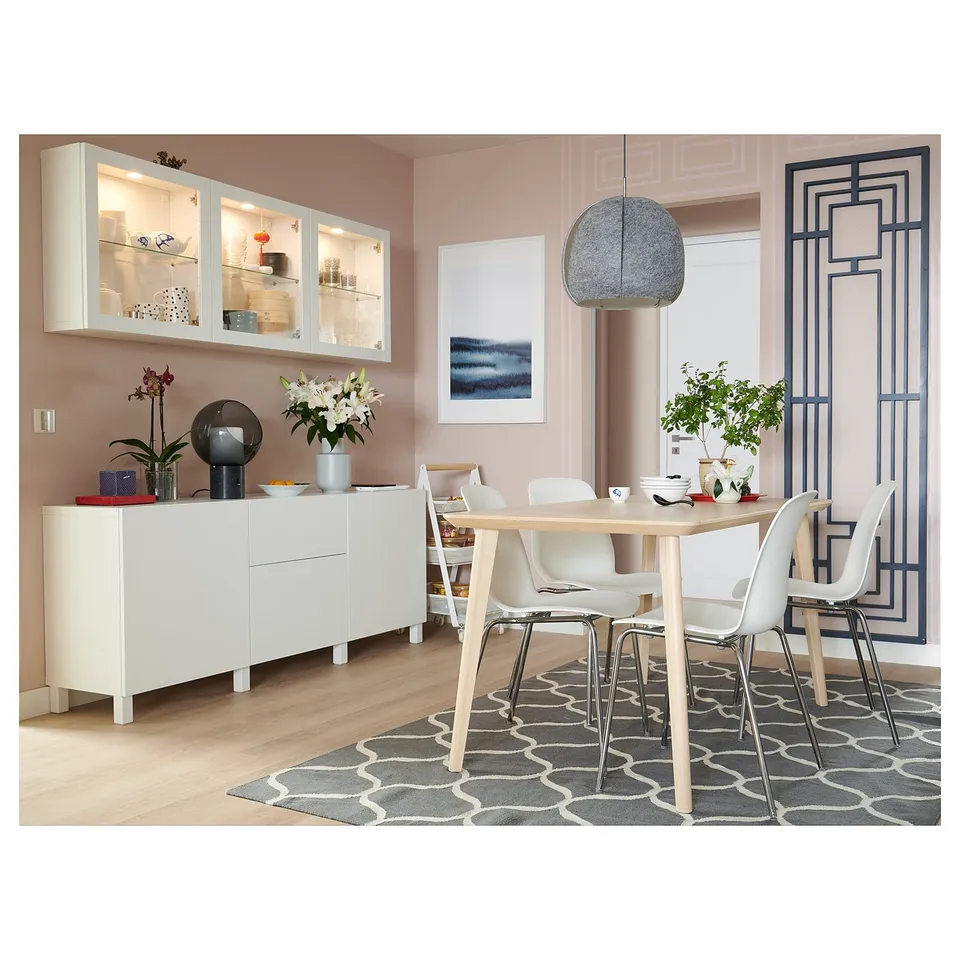 Modern dining room with white BESTÅ sideboard, light wood table, white chairs, grey rug, floral decorations, and abstract wall art.