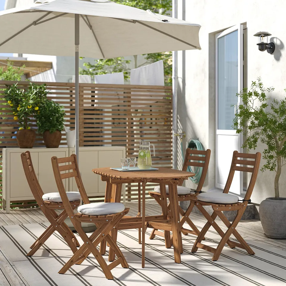 ASKHOLMEN: compact outdoor dining set with 4 foldable acacia wood chairs & table, light cushions, under beige umbrella.