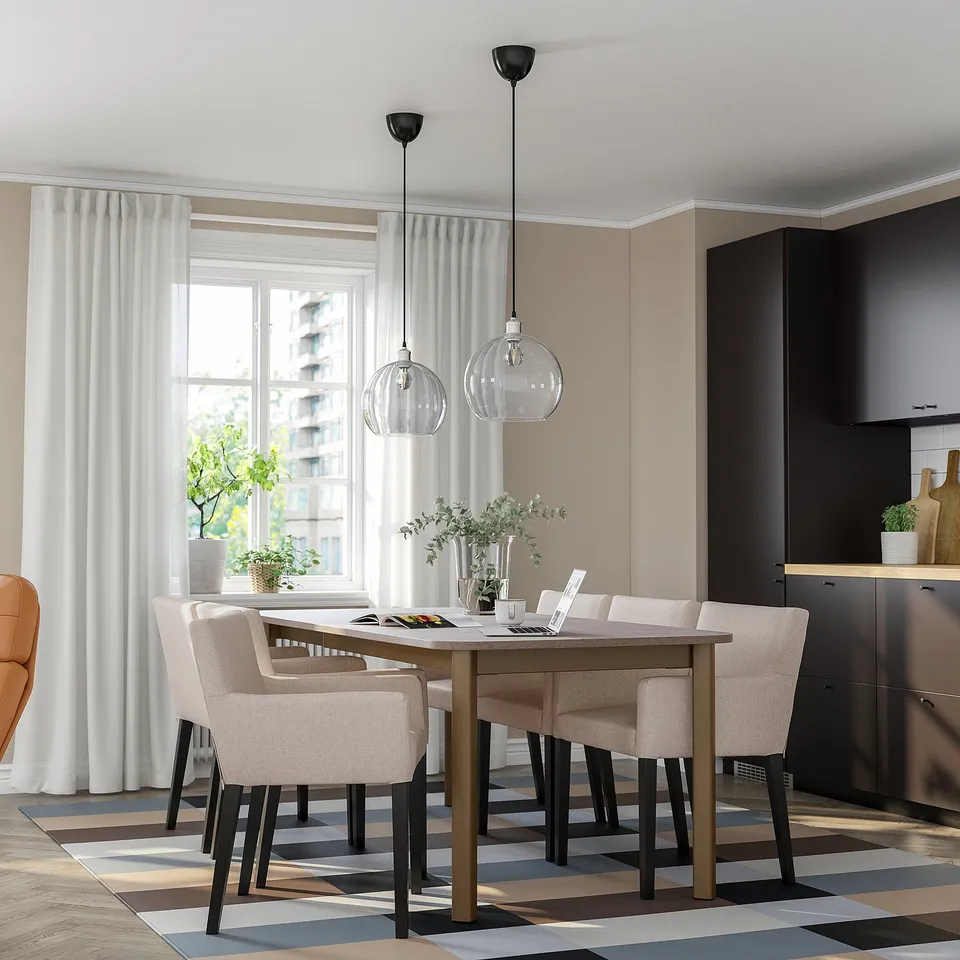 Modern dining room with beige STRANDTORP table, six chairs, pendant lights, multicoloured rug, plants, bright windows.