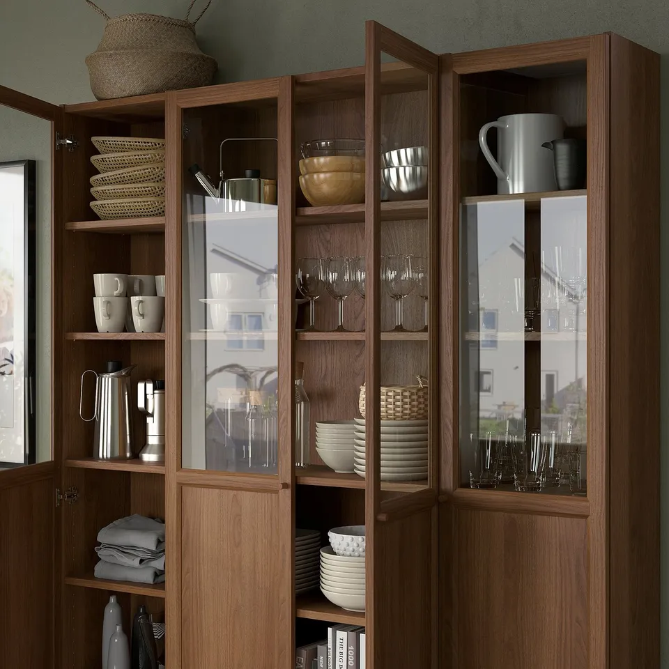 Wooden cabinet with glass doors displays dishes, glasses, mugs, and bowls neatly organised on several shelves.