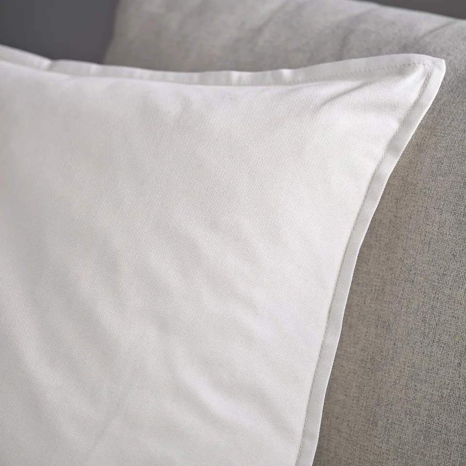 Close-up of soft, white pillowcase on a grey couch. Its smooth fabric quality and comfort.