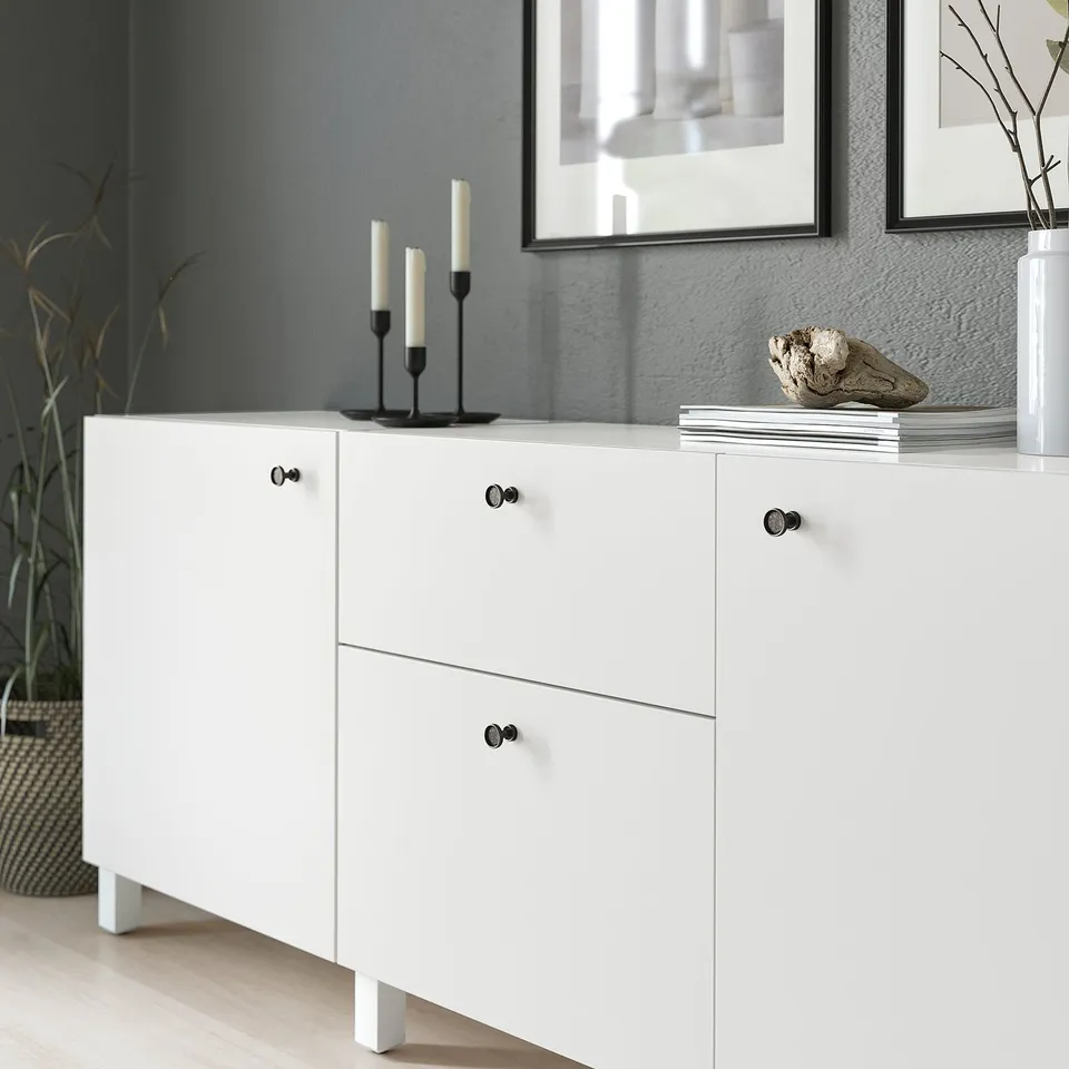White cabinet with anthracite knobs and handles, holding candles and decor accessories.