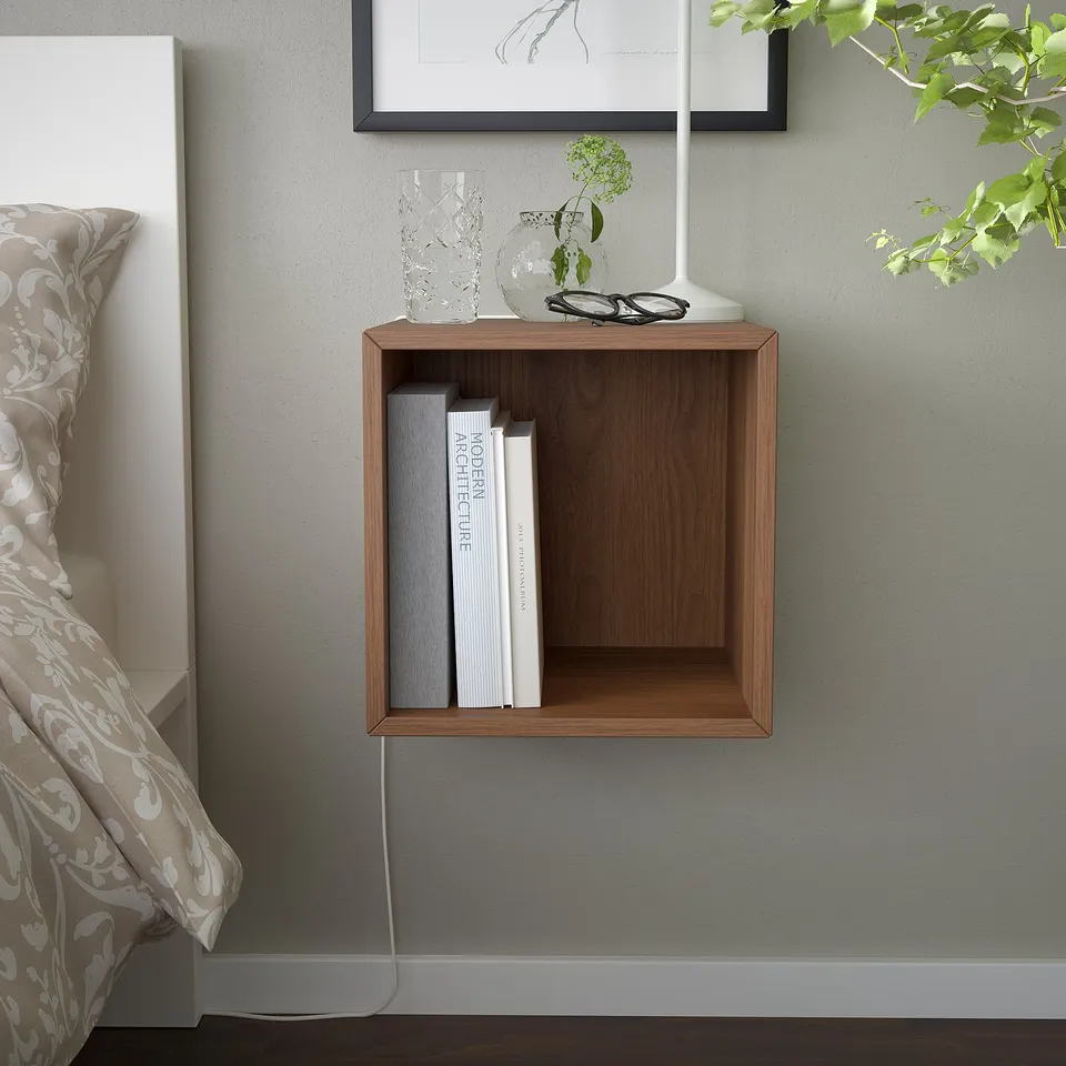 Wooden EKET shelf holds books by bed with beige comforter.