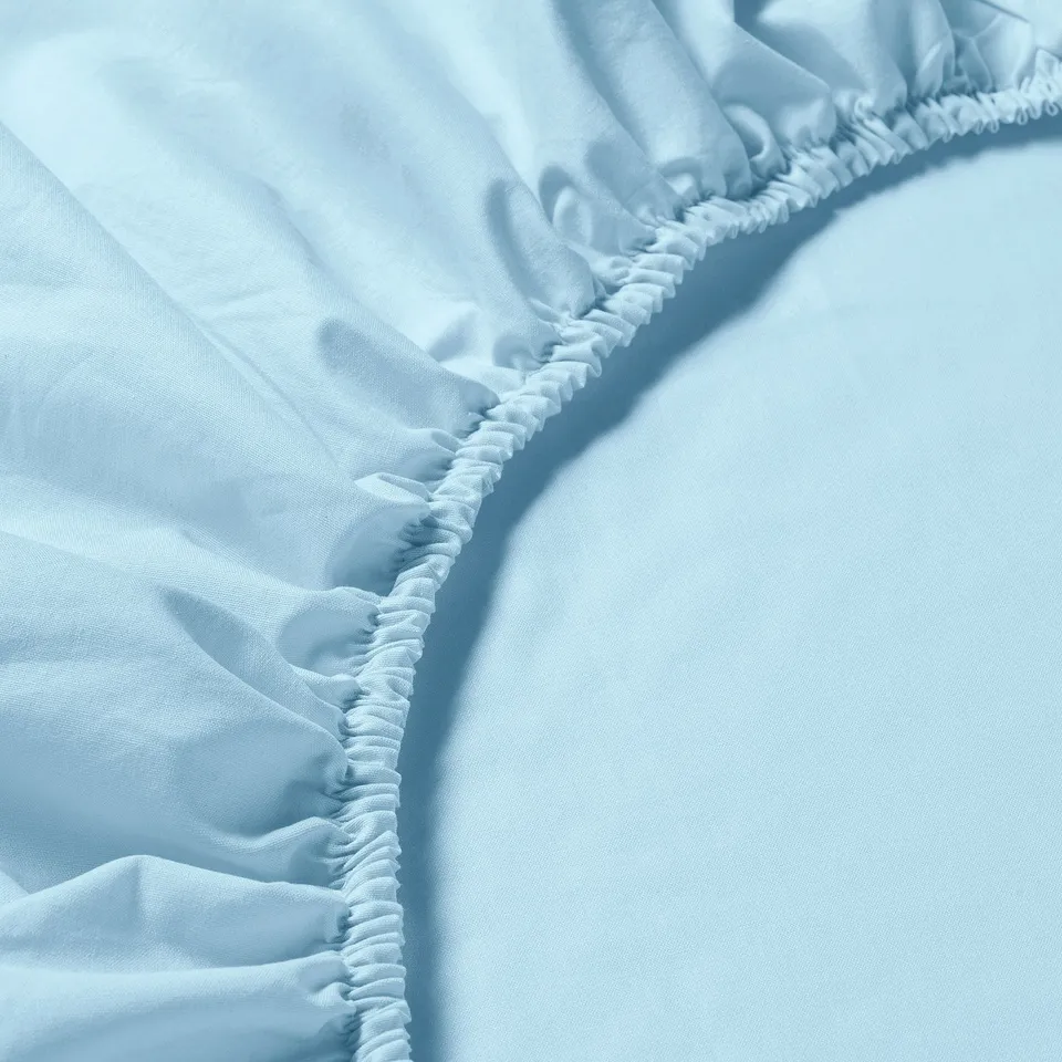Close-up of soft, light-blue DVALA cotton fitted sheet showing smooth texture and durable elastic edging.