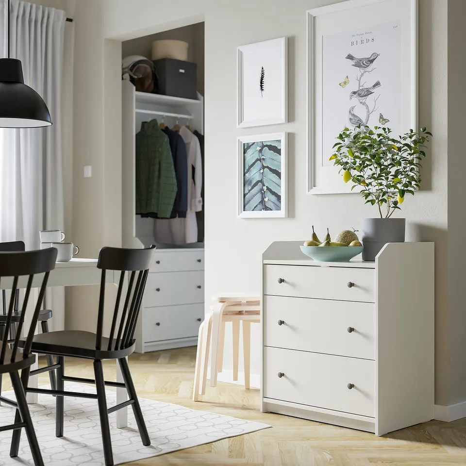 Cosy dining room featuring HAUGA white chest with 3 drawers, black chairs, grey curtains, and wall art.