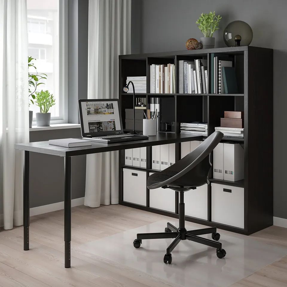 Home office setup with black INLÄGG desk against wall, featuring laptop, chair, and storage unit.
