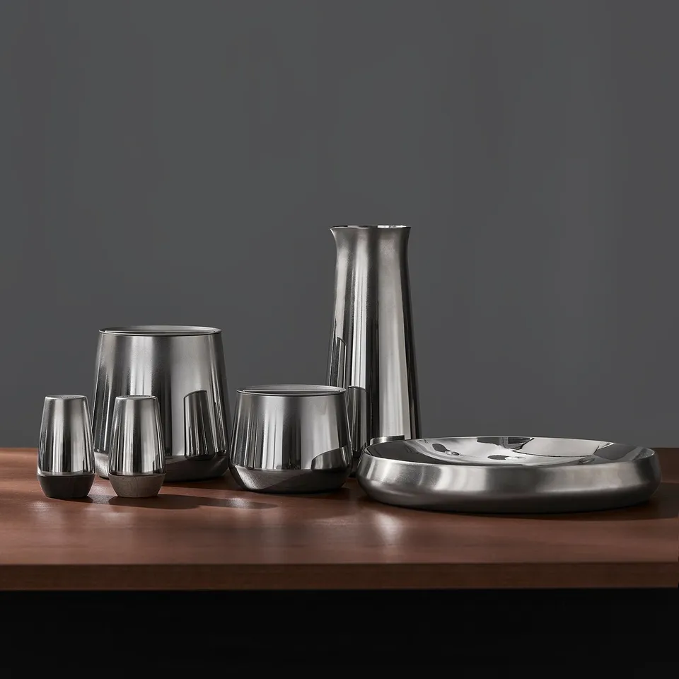 Modern steel carafe set with minimalist design. Includes pitcher and cups, perfect for cold drinks. Shiny surface and tactile finish.