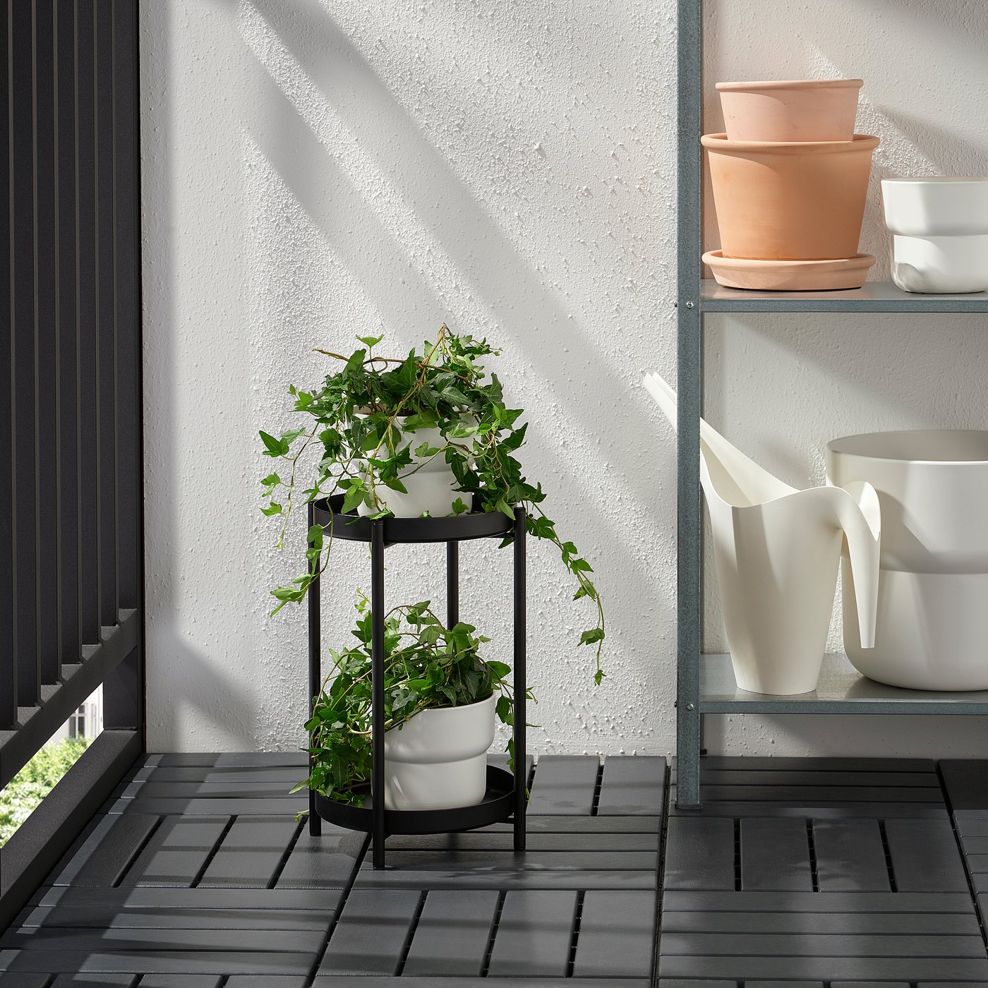 Balcony plant stand with stacked white pots and green plants on metal frame.