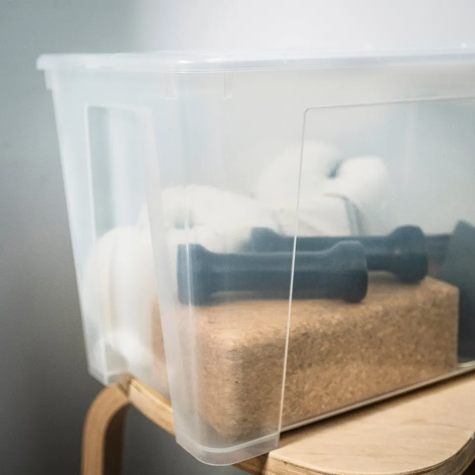 Clear plastic storage box with two dark blue handled items inside, placed on a wooden surface.