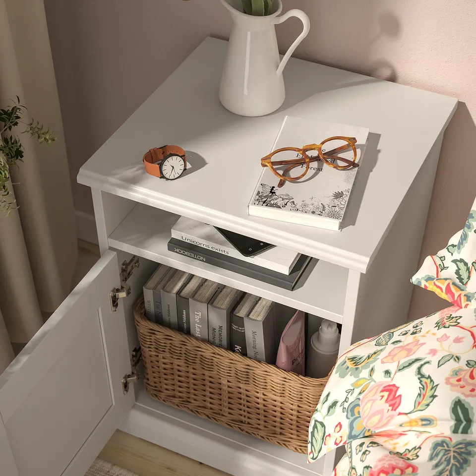 Small bedside table with a wicker basket storing books. A watch, glasses, and a vase on the top.