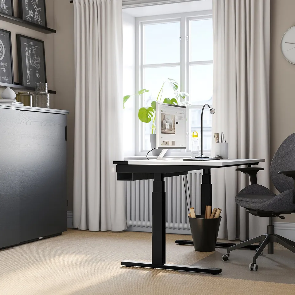 Modern home office setup featuring MITTZON desk in black with white top, grey chair, large window, and plant.